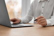 © New Africa - Woman with pen working on laptop at wooden table, closeup. Electronic document management