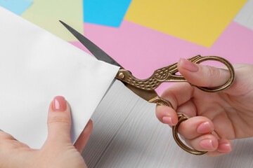 Canvas Print - Woman cutting paper with scissors at white wooden table, closeup