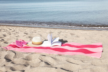 Wall Mural - Beach towel with book, slippers and straw hat on sand near sea