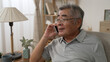 © PRPicturesProduction - Smiling asian old man talking on smartphone on sofa. Mature male in online conversation using mobile phone while laughing. cheerful elderly guy in glasses having fun during funny conversation call