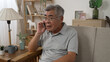 © PRPicturesProduction - shocked old asian man sitting on sofa and answer smartphone call while hearing bad news. confused grandpa in glasses worried about grandchildren while listening and talking on cellphone in apartment