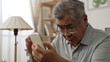 © PRPicturesProduction - Elderly asian male having eyesight problems and wearing eyeglasses while gazing and reading message on smartphone on sofa. Old man having eye blurred vision indoors and moving glasses up and down