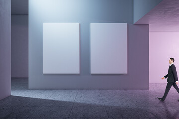 Poster - Side view of businessman walking in modern concrete gallery interior with mock up banners on wall and shadows.