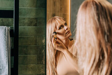 Blond Woman Applying Make-up With Brush In Bathroom
