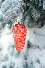 Orange Pine Cone Hanging On Branch Of Snow Covered Christmas Tree