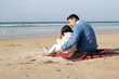 © KAMPUS - Happy Japanese family on blanket on beach. Father and daughter in casual clothes sitting on blanket, hugging. Family, relaxation, nature concept