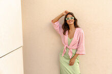 Positive Young Caucasian Woman Smiling With Teeth Posing At Camera Near Building Wall. Model Wears Shirt, Sundress And Sunglasses. Concept Of Stylish Vacation.