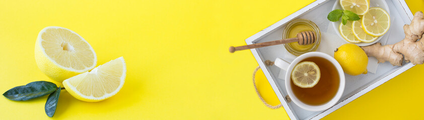 Wall Mural - Tea with lemon, honey and ginger on the white wooden tray on the yellow background. Copy space. Top view.