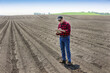 © Designpics - A farmer stands using a tablet on freshly tilled farmland; Alberta, Canada