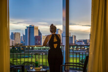 A Woman Relaxes And Looks At The Scenery Outside Of Her Hotel Room Window Over Downtown Bangkok, Thailand; Bangkok, Krung Thep Maha Nakhon, Thailand