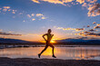 A woman runs along a lake reflecting the sunset.