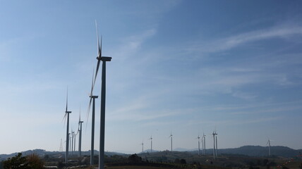 Wind farms generate electricity on the hill. Many wind turbines for generating electricity on bright blue sky background with selective focus copy space.