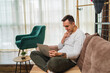 © Dusan - A young man using laptop drinking coffee and talking on phone at his home while also working