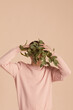 © TrueFrame Collective - Unrecognizable model wearing pale pink sweatshirt hiding his face behind branch with leaves