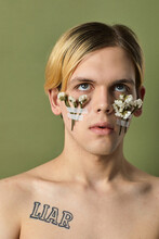 Portrait Of Topless Male Model With White Flowers Taped On His Cheeks