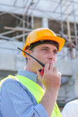 Wall Mural - American man technician Industrial engineer using walkie-talkie and holding blueprint working in construction site for building site survey in civil engineering project.