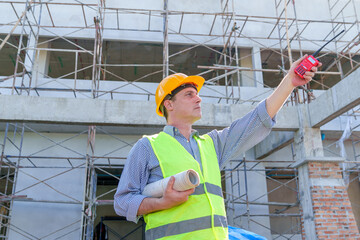 American man technician Industrial engineer using walkie-talkie and holding blueprint working in construction site for building site survey in civil engineering project.