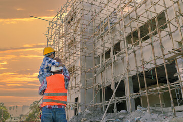 Wall Mural - Asian boy on father's engineer shoulder against the background of new high-rise buildings and construction cranes silhouette of cool sunset father and son concept