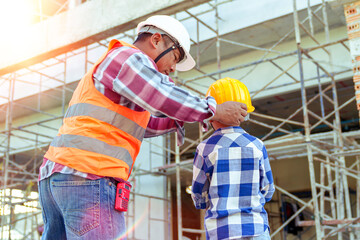 Wall Mural - Male contractor holding boy's hand standing looking at building under construction, father taking son to look at his construction site, low view from behind, father and son holding hands.