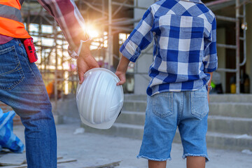 Wall Mural - Male contractor holding boy's hand standing looking at building under construction, father taking son to look at his construction site, low view from behind, father and son holding hands.