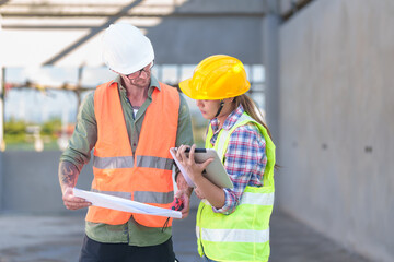 Wall Mural - Two professionals inspect construction site of commercial building, industrial building, real estate project  civil engineer, investor using laplet in background crane, skyscraper, concrete formwork