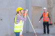 © ND STOCK - Construction Worker Using Theodolite Surveying Optical Instrument for Measuring Angles in Horizontal and Vertical Planes on Construction Site. Engineer and Architect Using blueprint Next to Surveyor.