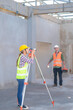 © ND STOCK - Construction Worker Using Theodolite Surveying Optical Instrument for Measuring Angles in Horizontal and Vertical Planes on Construction Site. Engineer and Architect Using blueprint Next to Surveyor.