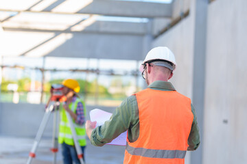 Wall Mural - Construction Worker Using Theodolite Surveying Optical Instrument for Measuring Angles in Horizontal and Vertical Planes on Construction Site. Engineer and Architect Using blueprint Next to Surveyor.