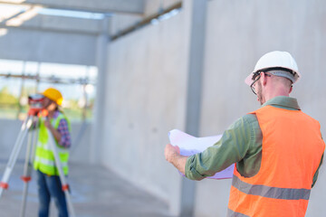 Wall Mural - Construction Worker Using Theodolite Surveying Optical Instrument for Measuring Angles in Horizontal and Vertical Planes on Construction Site. Engineer and Architect Using blueprint Next to Surveyor.