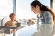 © Austockphoto - Mother and baby eating breakfast together in morning light with view out window over rooftops