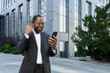 © Liubomir - African american businessman boss outside modern office building using phone, senior man celebrating victory success reading good news online from smartphone, holding hand up gesture of triumph .