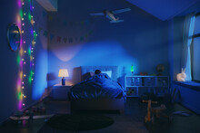 3d Rendering Of An Atmospheric Children Room In The Night. A Boy Is Sleeping In Bed With Colorful Lights, Toys And Moonlight Lighting Blue The Room.