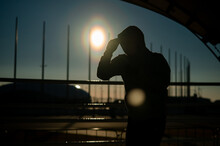 A Man In A Sweatshirt Trains In Boxing At The Stadium At Sunset. Athlete Silhouette.