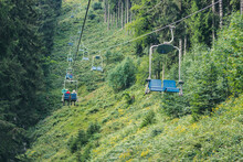 Cable Car, Ski Lift With Blue Seats In Summer Among The Green Pine Trees