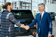 © Iryna - Happy car salesman and male customer in auto dealership, they are shaking hands seal the purchase of the auto or new car.