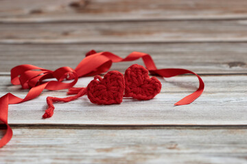 two handmade crochet hearts and red ribbon on wooden background.  Love concept background, wallpaper, banner with space for writting. Valentines or mother day background.