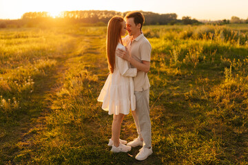 Wall Mural - side view of loving young couple hugging and kissing standing on beautiful green meadow in summer ev