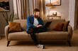 © Drobot Dean - Smiling man using laptop while sitting on couch in cozy living room