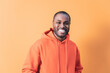 ©  Yistocking - An adult dark-skinned man laughing while looking at the camera. The young man is wearing an orange hooded sweatshirt to match the background.