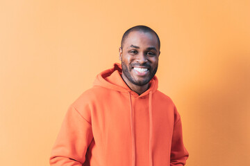 An adult dark-skinned man laughing while looking at the camera. The young man is wearing an orange hooded sweatshirt to match the background.