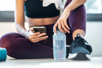 Wall Mural - Sporty woman using her mobile phone while holding water bottle after a pilates class at home.