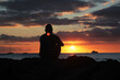 Man sitting alone on beach rocks looking at the sunset, lost in thought