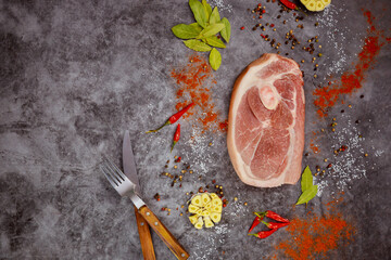 Wall Mural - On dark background, raw pork chops are arranged with spices and fork.