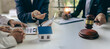 © ArLawKa - Judge holding wooden judge hammer against house background and businessman documents and house model on wooden table Real estate disputes and property auction concept