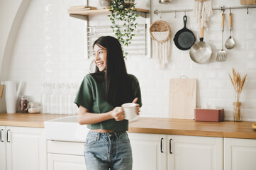 Poster - Happy young asian woman smile and relax in kitchen at home. Female resting weekend at house