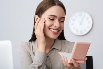 Poster - Young woman looking at herself in cosmetic pocket mirror indoors