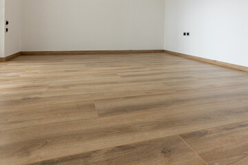 Laminated wood floor with white wall. Empty room with floating laminate in new apartmen