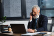 © LIGHTFIELD STUDIOS - Cheerful mature businessman talking on cellphone near laptop and coffee to go in office in evening