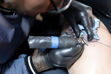 Fototapeta Konie - A tattoo artist is tattooing a snake and a rose on a woman's leg. Close up.