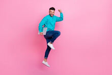 Full Size Photo Of Young Nice Guy Jumping Hold Laptop Raise Fist Successful Worker Wear Trendy Blue Look Isolated On Pink Color Background